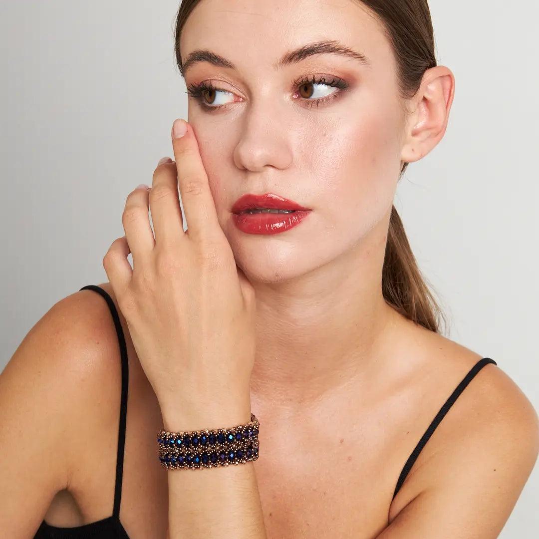 A close-up view of a woman's wrist wearing a handmade bracelet with shimmering dark blue crystal beads and a detailed copper clasp,
showcasing elegance and artisanal craftsmanship. Perfect for both casual and formal occasions.