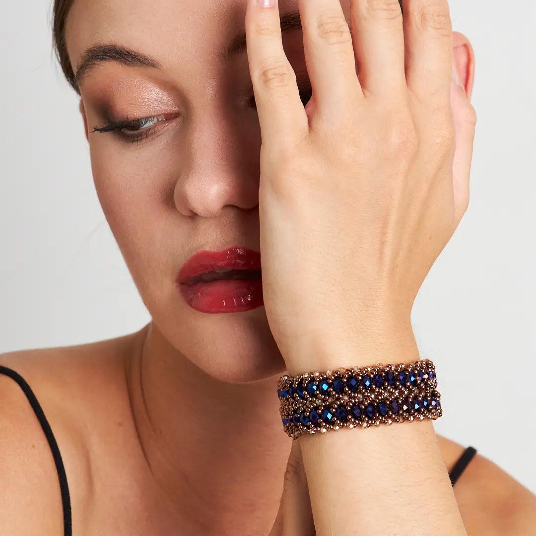 A close-up view of a woman's wrist wearing a handmade bracelet with shimmering dark blue crystal beads and a detailed copper clasp, showcasing elegance and artisanal craftsmanship. Perfect for both casual and formal occasions.