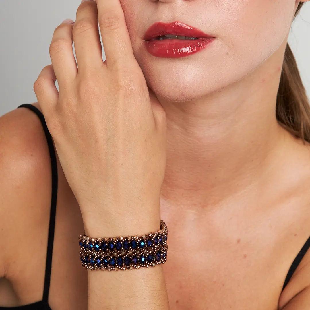 A close-up view of a woman's wrist wearing a handmade bracelet with shimmering dark blue crystal beads and a detailed copper clasp, showcasing elegance and artisanal craftsmanship. Perfect for both casual and formal occasions.